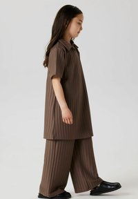 Hnědý pruhovaný dvoudílný outfit obsahující tričko s krátkým rukávem a kalhoty s širokými nohavicemi. Doplněno černými nazouvacími botami, což dodává texturovaný vzhled.
