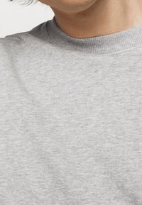 Sudadera gris con un tejido texturizado, cuello redondo y sutiles variaciones de color, presentada desde el área superior del pecho.