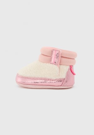 Soft baby bootie in cream fleece with metallic pink trim and cuff, featuring a shiny pink pull tab on the heel.