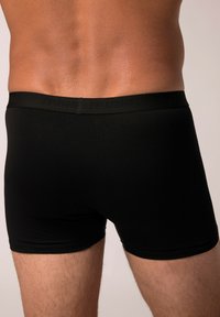 Boxer neri in cotone con una texture liscia, dotati di un elastico con l'etichetta "JP1880" in nero. La vestibilità è aderente, arrivando fino a metà coscia.