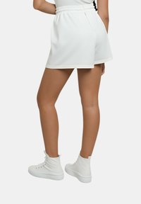 Pantaloni corti bianchi con vita elasticizzata, caratterizzati da un design semplice e bordi a contrasto. Indossati con sneakers bianche alte alla caviglia.