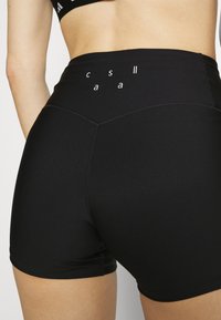 Black athletic shorts with a high waist, made from stretchy fabric. Features flat seams and white text accents near the waistband.