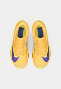 Nike skriešanas apavi ar sietu augšu spilgti dzeltenā krāsā un purpura akcentiem. Iekļauti dzīvīgu krāsu šņores un mīksts zoleē komfortam.