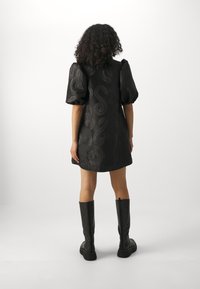 Schwarzes Kleid mit ballonartigen Ärmeln, das ein strukturiertes Paisley-Muster aufweist. Kombiniert mit kniehohen schwarzen Stiefeln für einen Kontrast.