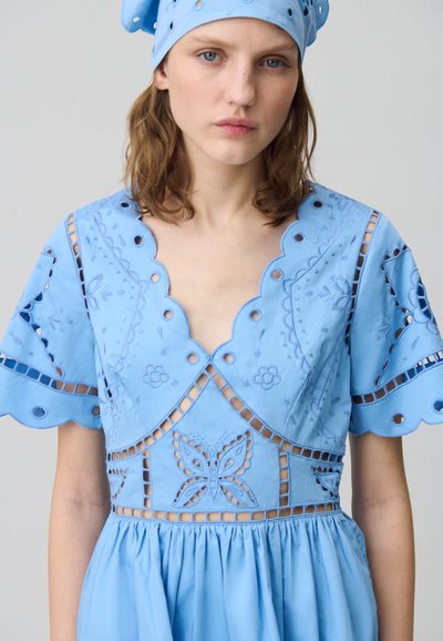 Vestido azul claro con bordados florales y detalles calados; mangas de volantes y un escote en V, complementado con un pañuelo a juego.