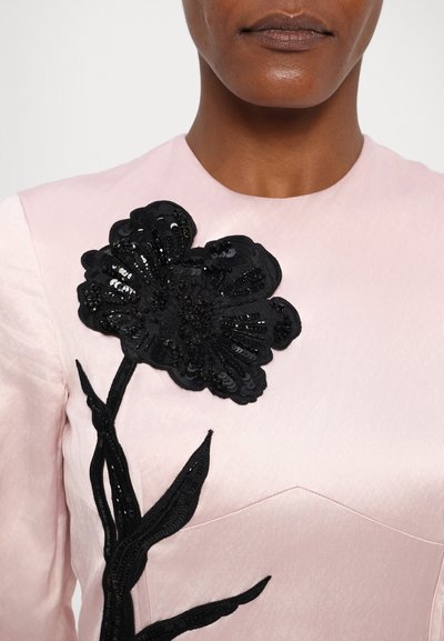 Pink satin top featuring a black sequined floral appliqué, with black embroidered leaves extending down the side. Smooth texture.