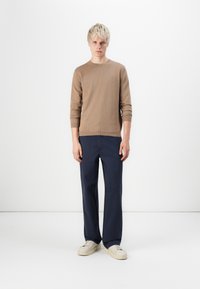 Brown knitted sweater with long sleeves, paired with navy wide-leg trousers. Footwear is off-white with a textured sole. Simple, clean design.