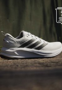 Chaussure de running blanche Adidas avec des bandes noires, semelle blanche épaisse portant la mention "DREAMSTRIKE" et texte "SUPERNOVA" sur le côté.