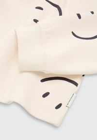 Lyscreme sweatshirt med sort smiley-ansigt trykt design. Ribbet manchetter og kant. Etiketten på undersiden læser "Tom Tailor."