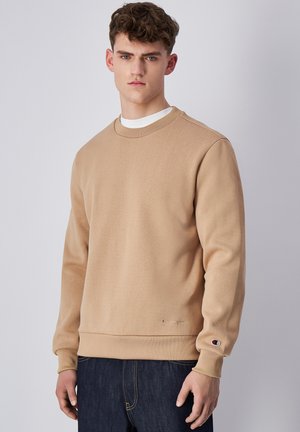 Sudadera de cuello redondo en color beige hecha de tejido texturizado, con puños y dobladillo de canalé, y un pequeño logotipo en la manga izquierda.