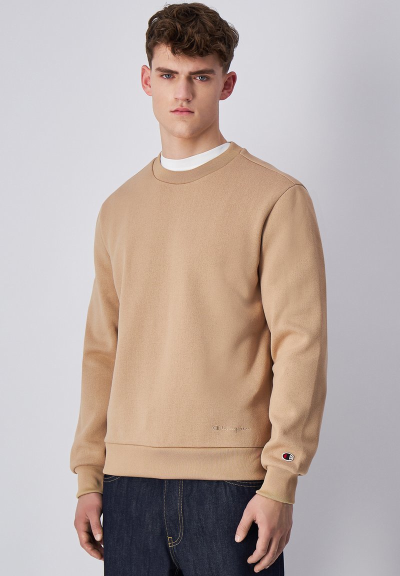 Sudadera de cuello redondo en color beige hecha de tejido texturizado, con puños y dobladillo de canalé, y un pequeño logotipo en la manga izquierda.