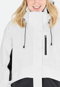 Weiße und schwarze wasserdichte Jacke mit hohem Kragen, verstellbaren Kordeln und einer mit Reißverschluss versehenen Brusttasche. Glatte Textur, modernes Design.