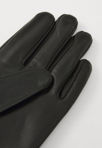 Sorte læderhandsker med glat tekstur, femfingerdesign og subtile stikninger over sømmene.