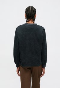 Ciemnoszara bluza z teksturowaną powierzchnią, opuszczonymi ramionami i ściągaczami na rękawach. Tył z okrągłym dekoltem i luźnym krojem.