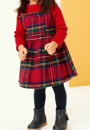 Robe à carreaux rouges avec une jupe évasée et des boutons en accent, associée à des collants en maille bleu marine et des bottines noires. Texture de tissu douce.