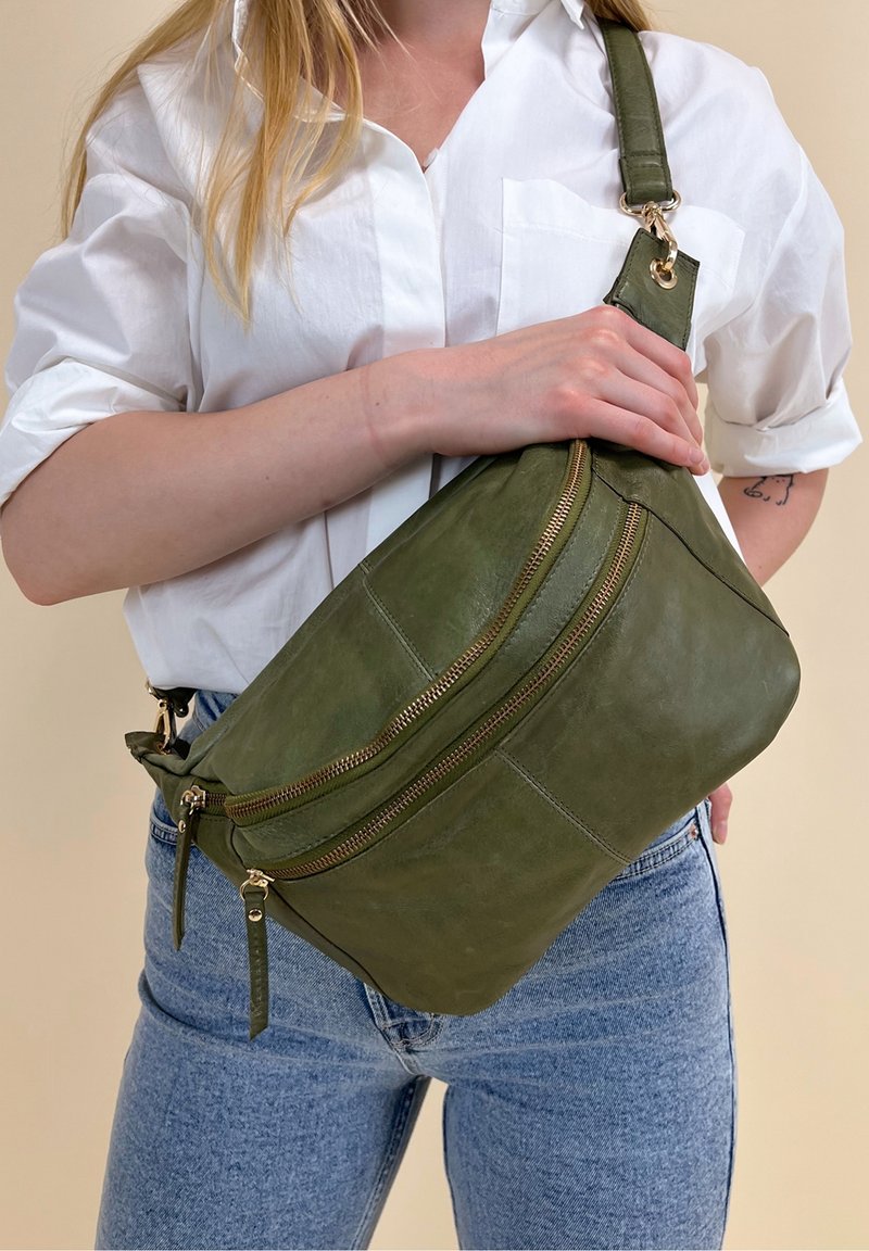 Borsa a tracolla verde in pelle con due scomparti con zip e una larga tracolla regolabile. Texture liscia e dettagli in metallo dorato lucido.