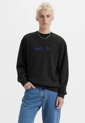 Felpa nera con logo ricamato "LEVI's" blu, scollo rotondo, maniche lunghe e vestibilità rilassata, abbinata a jeans azzurri chiari.
