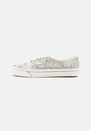 Baskets basses blanches avec un motif craquelé noir, des lacets blancs et une semelle en caoutchouc blanche épaisse sur un fond uni.