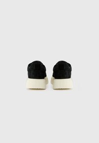 Pair of black suede sneakers with thick white ribbed soles, viewed from the back, against a plain light background.