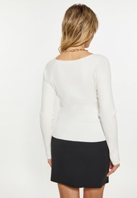 Top bianco a maniche lunghe con colletto ampio, abbinato a una gonna nera corta. Tessuto texturizzato con una silhouette aderente.
