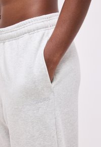 Χέρι στην τσέπη γκρι ανοιχτού χρώματος φόρμας με ελαστική μέση και διακριτικό λογότυπο «BORG», φορεμένη από άτομο με σκουρόχρωμο δέρμα.