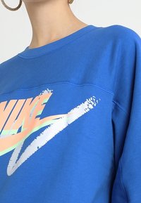 Blå sweatshirt i ett blandat bomullstyg, utrustad med en djärv, flerfärgad Nike-logotyp med en penseldragdesign över bröstet.