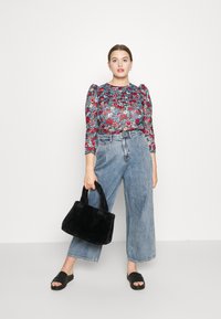 Top floreale a maniche lunghe con dettagli arricciati, abbinato a jeans a gamba larga in denim blu chiaro a vita alta. Borsa nera in pelliccia e sandali neri.