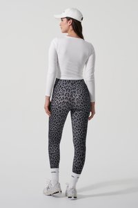Schwarze und graue Leopardenmuster-Leggings aus dehnbarem Stoff, kombiniert mit einem weißen, taillierten Langarmoberteil und einer weißen Kappe.