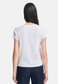 Vit kortärmad topp med rundad halsringning och en slät, mjuk textur. Har raglanärmar och en avslappnad passform.