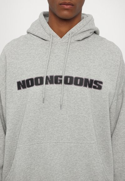 Felpa grigia con un grande logo nero "NOONGOONS" sul petto, cordini al collo e un tessuto morbido e testurizzato.