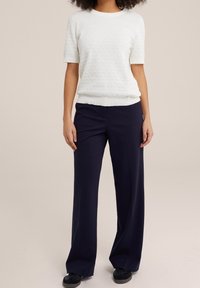 Pull court en maille légère de couleur blanche, associé à un pantalon large taille haute navy et des chaussures noires. Design simple et épuré.