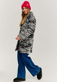 Chlpatý kabát s čierno-bielym zvieracím vzorom, skombinovaný s voľnými modrými džínsami a jasne ružovou rebrovanou čiapkou. Čierna obuv dopĺňa vzhľad.