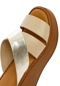 Lichtbeige platform sandaal met twee brede banden, één in metallic zilver en een gestructureerde bruine rubberen zool voor extra grip.