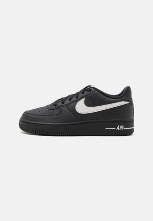Zapatilla de cuero negra con un logo Swoosh blanco, puntera redondeada, parte superior perforada y una suela de goma gruesa con la palabra "AIR" en letra blanca.