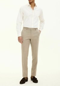 Beige skräddarsydda byxor med en slät textur, med en platt framsida, bälteshällor och en enkel knappstängning, parat med en ljusfärgad skjorta.