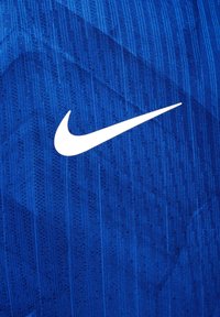 Logo blanc Nike Swoosh centré sur un tissu de sport bleu texturé avec des motifs subtils verticaux et diagonaux.
