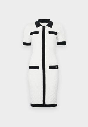 Balta suknelė su tekstūruotu raštu, trumpomis rankovėmis, juodu apykakle ir akcentais, priekinė užtrauktukas ir dvi juodos kišenės priekyje.