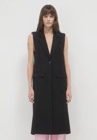 Schwarze ärmellose Weste mit tiefem V-Ausschnitt, vorderem Knopfverschluss und zwei Seitentaschen, die ein sauberes, maßgeschneidertes Design aufweist.