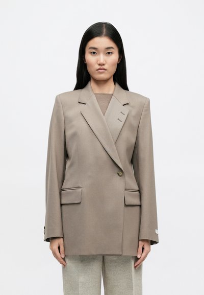 Μπεζ σακάκι διπλής όψης με μακριά μανίκια, κοφτές πέτες, δύο μπροστινές τσέπες, κούμπωμα με κουμπιά και διακριτές ραφές.