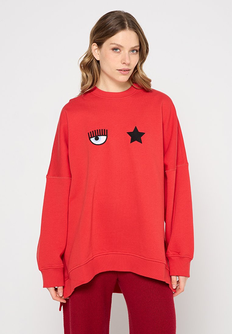 Czerwona, oversize bluza z miękkiego materiału, z nadrukiem niebieskiego oka i czarnego wzoru gwiazdy z przodu. Luźny krój i okrągły dekolt.
