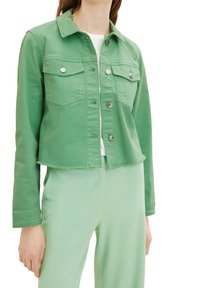 Giacca di jeans verde a crops con due tasche sul petto, dettagli in bottone argentato e orlo sfrangiato. Abbinata a pantaloni abbinati di un verde chiaro.