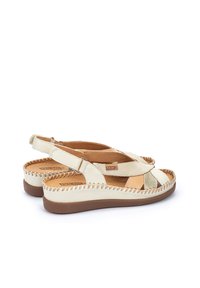 Sandalias de cuero de color claro con un diseño trenzado, correa trasera ajustable y suela gruesa de goma marrón. Costura decorativa a lo largo del borde.
