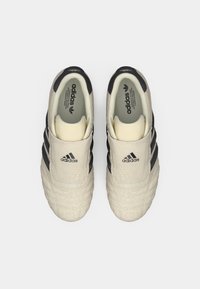 Λευκά sneakers με υφή, μαύρες ρίγες και ελαστική εφαρμογή. Το λογότυπο και η σήμανση είναι ορατά στη γλώσσα και στις εσωτερικές σόλες. Λαστιχένια σόλα.