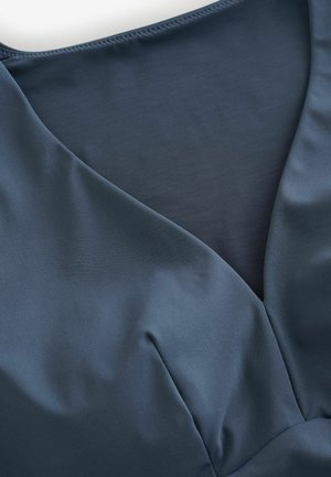 Dunkelblaues V-Ausschnitt-Kleidungsstück aus glattem Stoff mit einem transparenten Netz-Einsatz unter dem Ausschnitt, der einen Kontrast in der Textur zeigt.