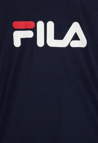 Jūras zilas sporta krekls ar sietveida tekstūru, ar lielu baltu "FILA" logotipu un mazu sarkanu akcentu virs burtu "F".