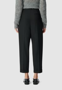 Hoge taille, los zittende zwarte broek met omgeslagen broekspijpen, voorzien van een subtiele achterzak, gecombineerd met een zachte grijze gebreide trui.