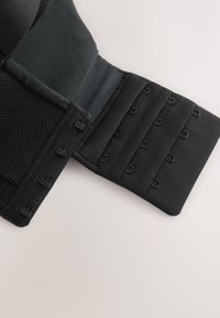 Chiusura per capo d'abbigliamento in tessuto nero con tre file di ganci e occhielli per chiusura regolabile, mostrata aperta su sfondo chiaro.