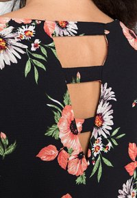 Schwarzes Blumenkleid mit ausgeschnittenem Rücken und zwei horizontalen Trägern. Der Stoff zeigt rosa und weiße Blumen mit grünen Blättern.