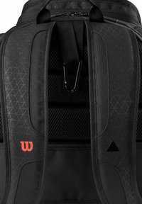Sac à dos noir avec un tissu texturé, rembourrage en maille sur les bretelles, motif géométrique, logo rouge et bretelles réglables avec un mousqueton.