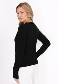 Pulover negru cu un design ajustat, mâneci lungi și gât rotund. Prezintă un accent alb la guler. Textură fină.